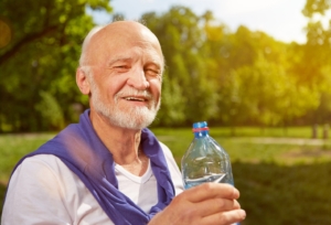 Durstiger Senior trinkt Wasser im Sommer aus einer Flasche in der Natur