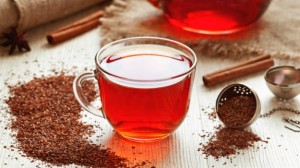 Cup of healthy traditional herbal rooibos red beverage tea with spices on vintage wooden table